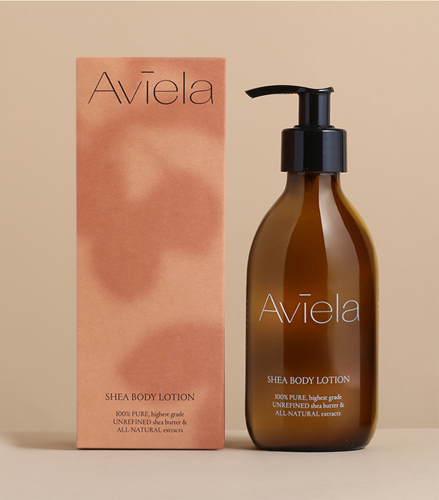 A product shot of Aviela Shea Body Lotion. A rectangular, peach-colored box stands next to a brown glass bottle with a black pump dispenser. The box and the bottle both have the product name and a description of the ingredients, which include "100% PURE, highest grade UNREFINED shea butter & ALL-NATURAL extracts."