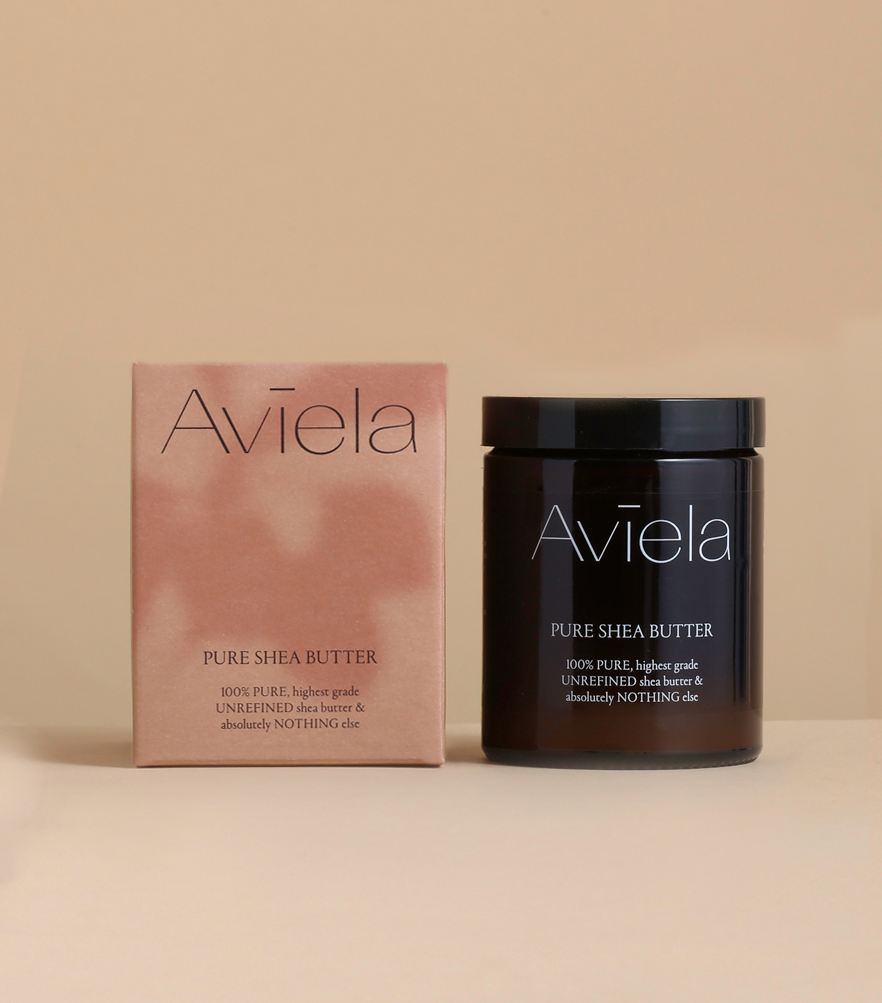 A product shot of Aviela Shea Body Butter Duo pack. A rectangular, peach-colored box stands next to a dark brown jar with a black lid. The box and the jar both have the product name and a description of the ingredients, which include "100% PURE, highest grade UNREFINED shea butter & ALL-NATURAL extracts."