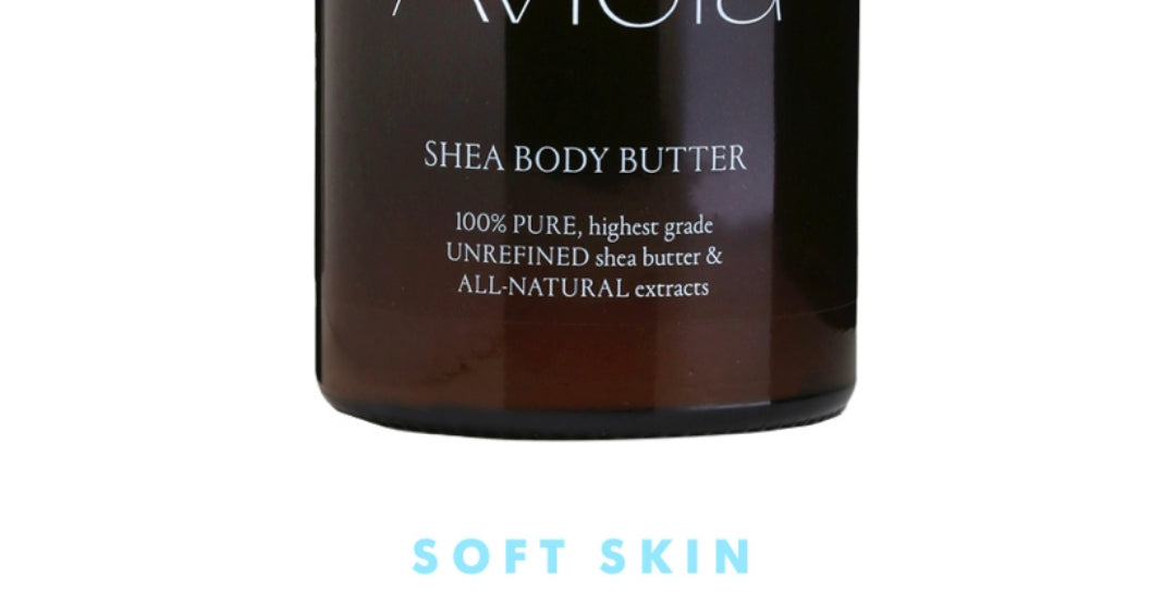 A close-up of a brown jar of Aviela Shea Body Butter. The label text is white and reads: "SHEA BODY BUTTER," followed by "100% PURE, highest grade UNREFINED shea butter & ALL-NATURAL extracts." Below the jar, the words "SOFT SKIN" are written in a light blue color.