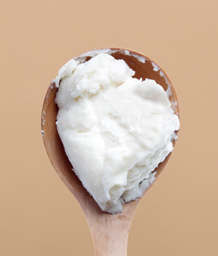 An image of a wooden spoon with a scoop of a thick, white, creamy pure shea butter. The background is a solid, light tan color.