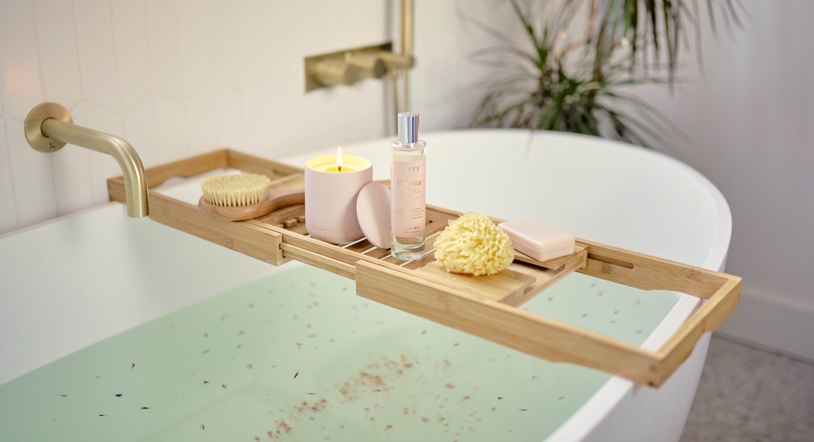 Image of a full bath with petals in the water and pamper products on the side 